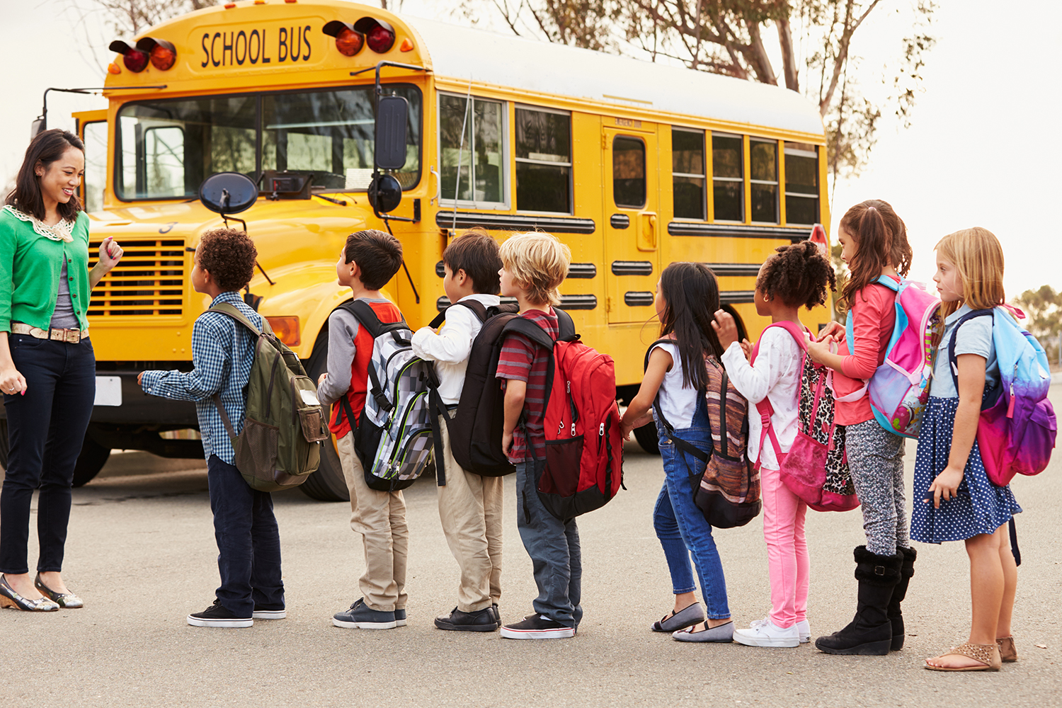 students lined up in front of a bus with a teacher