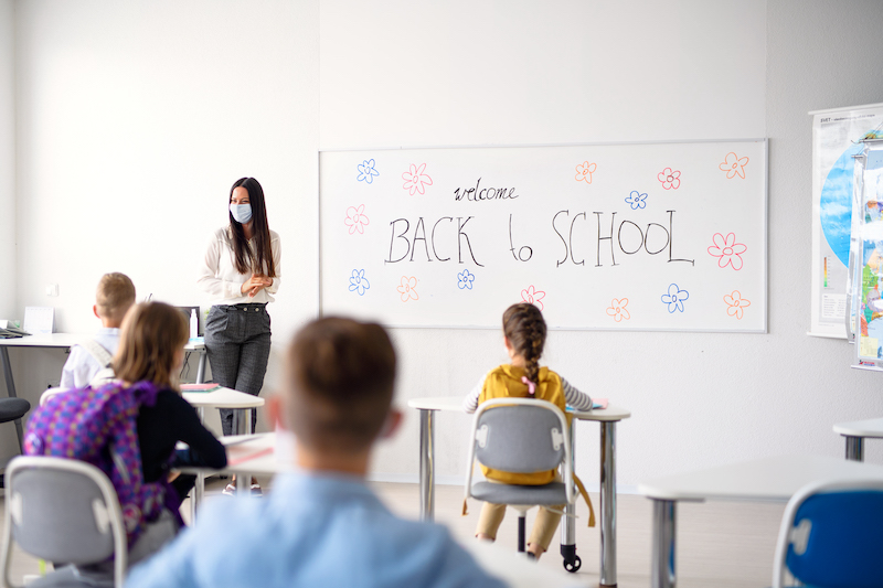 teacher-with-face-mask-welcoming-children-back-at